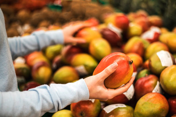 Young woman choose fresh mango at supermarket, hand close up